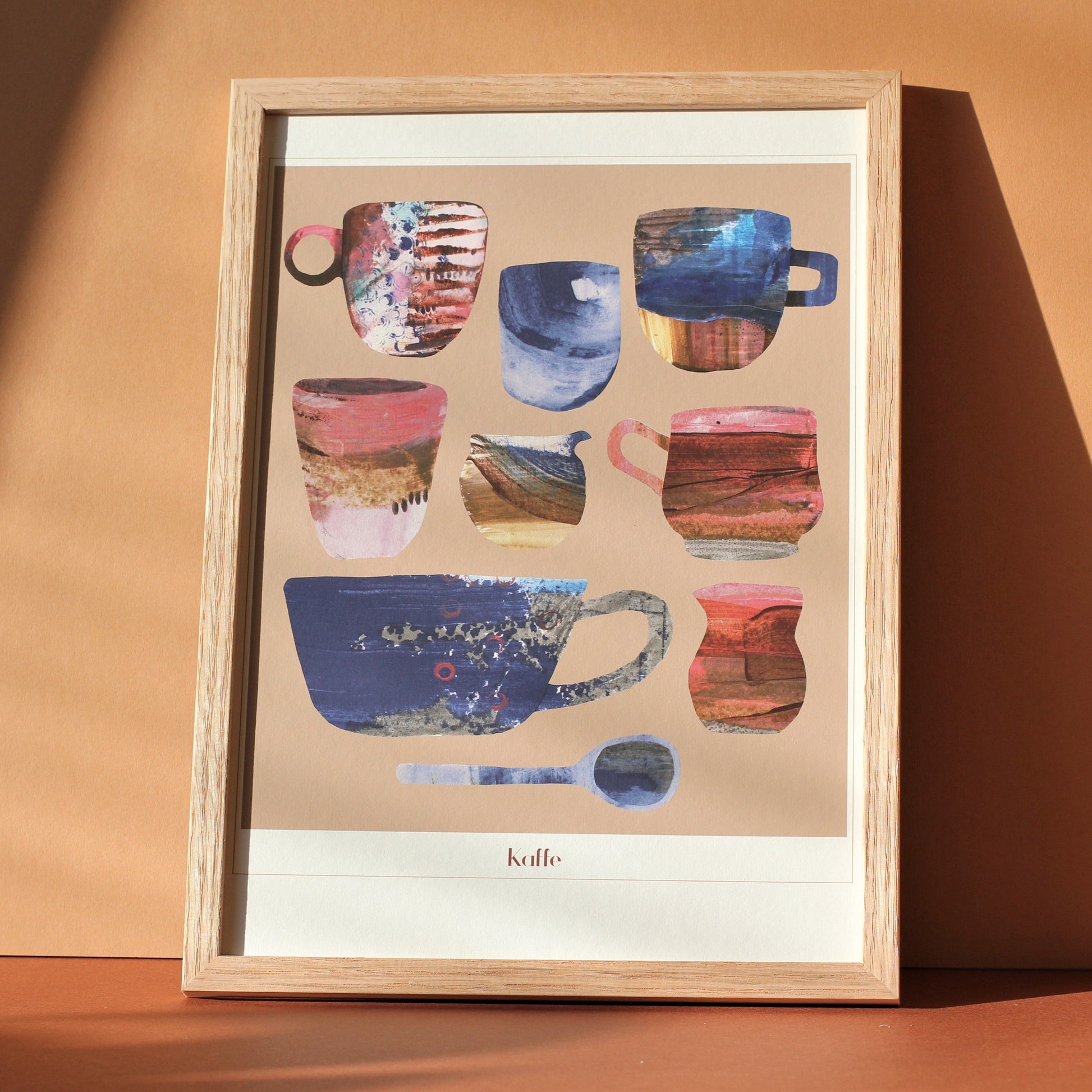 An art print for coffee lovers. The print shows a group of retro coffee cups, jugs and spoons in pinks, browns and china blues against a sand coloured background. The print is photographed framed in a sunny room.