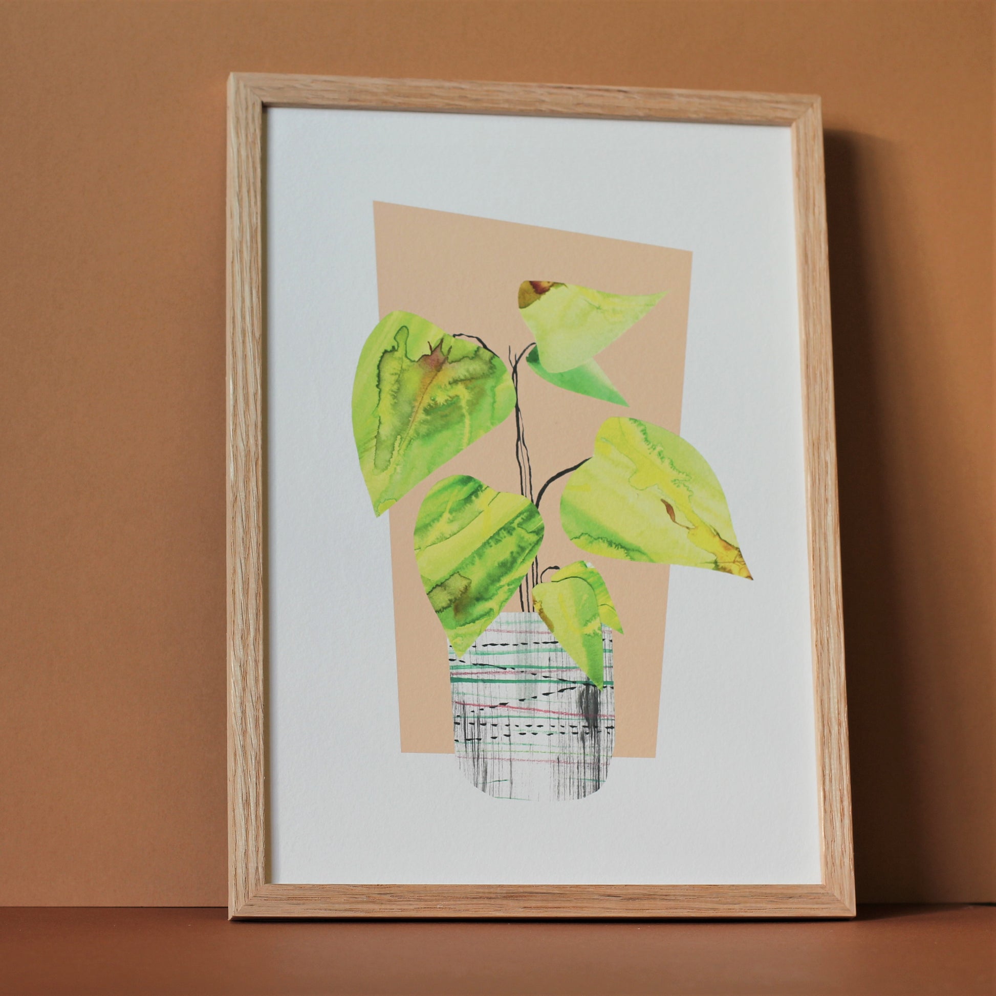 A midcentury modern style art print of a tropical houseplant in a pot against a peach background. The print is photographed in a wooden frame against a neutral background.