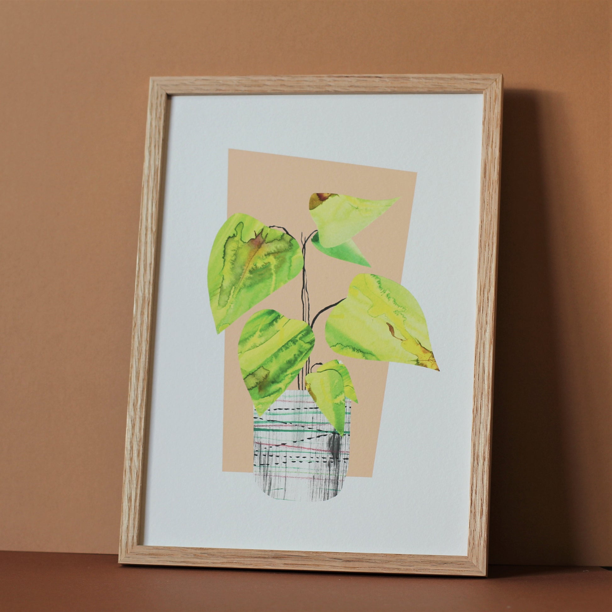 A midcentury modern style art print of a tropical houseplant in a pot against a peach background. The print is photographed in a wooden frame against a neutral background.