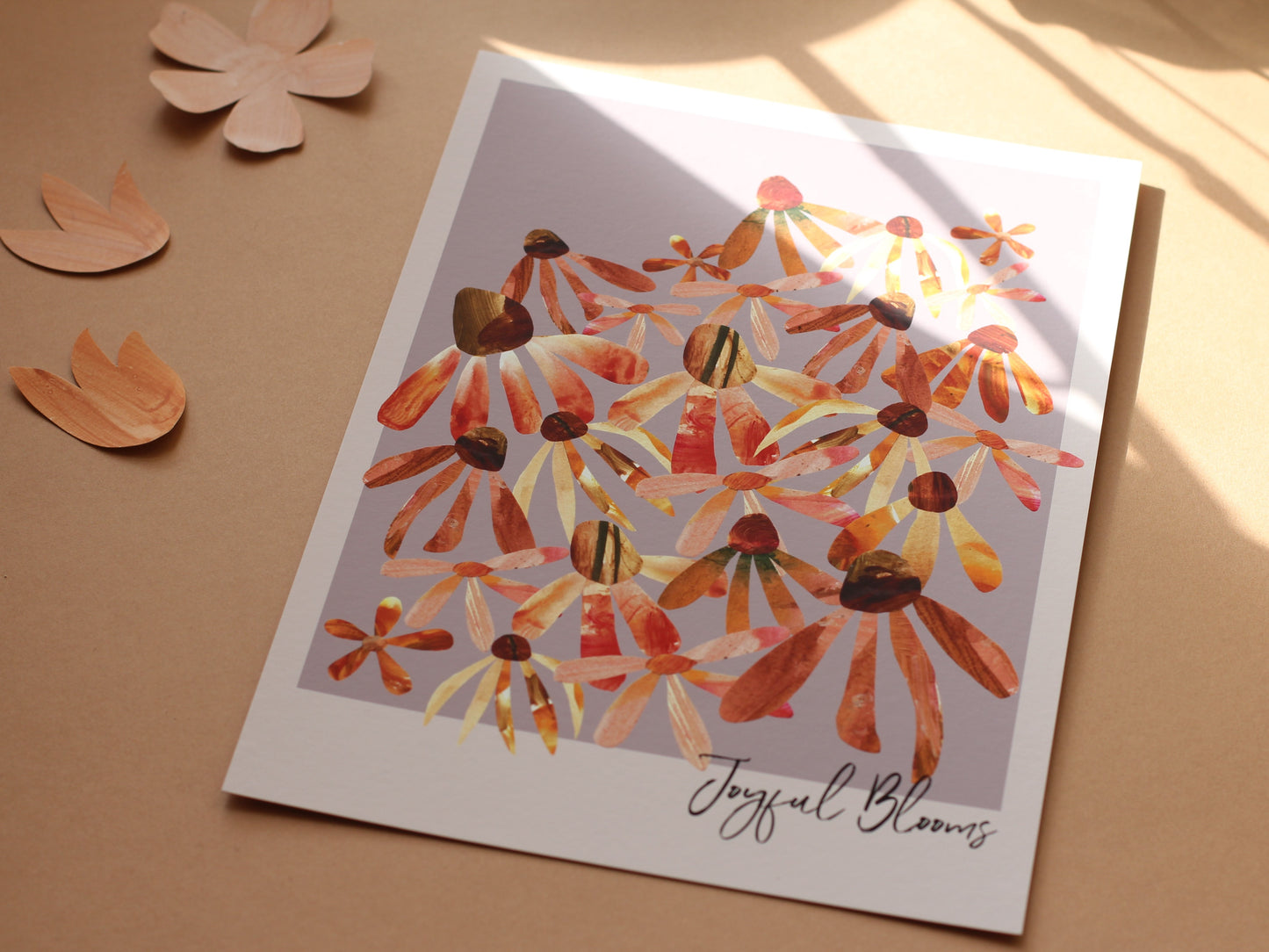 A floral art print of echinacea and daisy flower heads in oranges and pinks against a lilc background. The print is photographed against a sunny peach background.